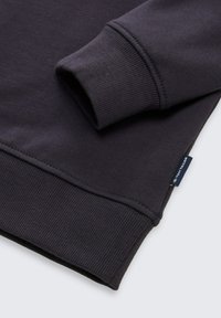 Sweatshirt gris foncé avec des poignets et un ourlet côtelés, texture douce, et une petite étiquette de marque cousue sur le côté.