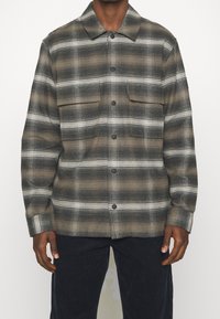 Grå och svart rutig skjorta med knäppning fram, två bröstfickor och spetsig krage. Mjuk textur och avslappnad passform.