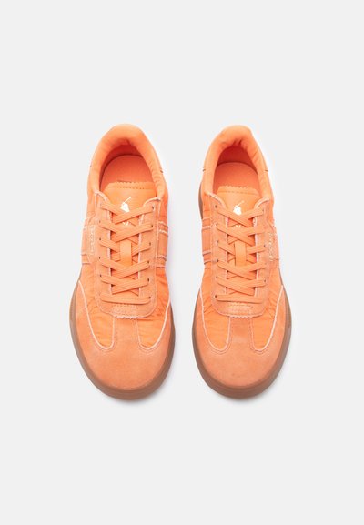 Ζευγάρι πορτοκαλί αθλητικά παπούτσια με κορδόνια, με σουέτ καλύμματα στα δάχτυλα και σόλες από καουτσούκ χρώματος τσίχλας, που φαίνονται από ψηλά σε λευκό φόντο.