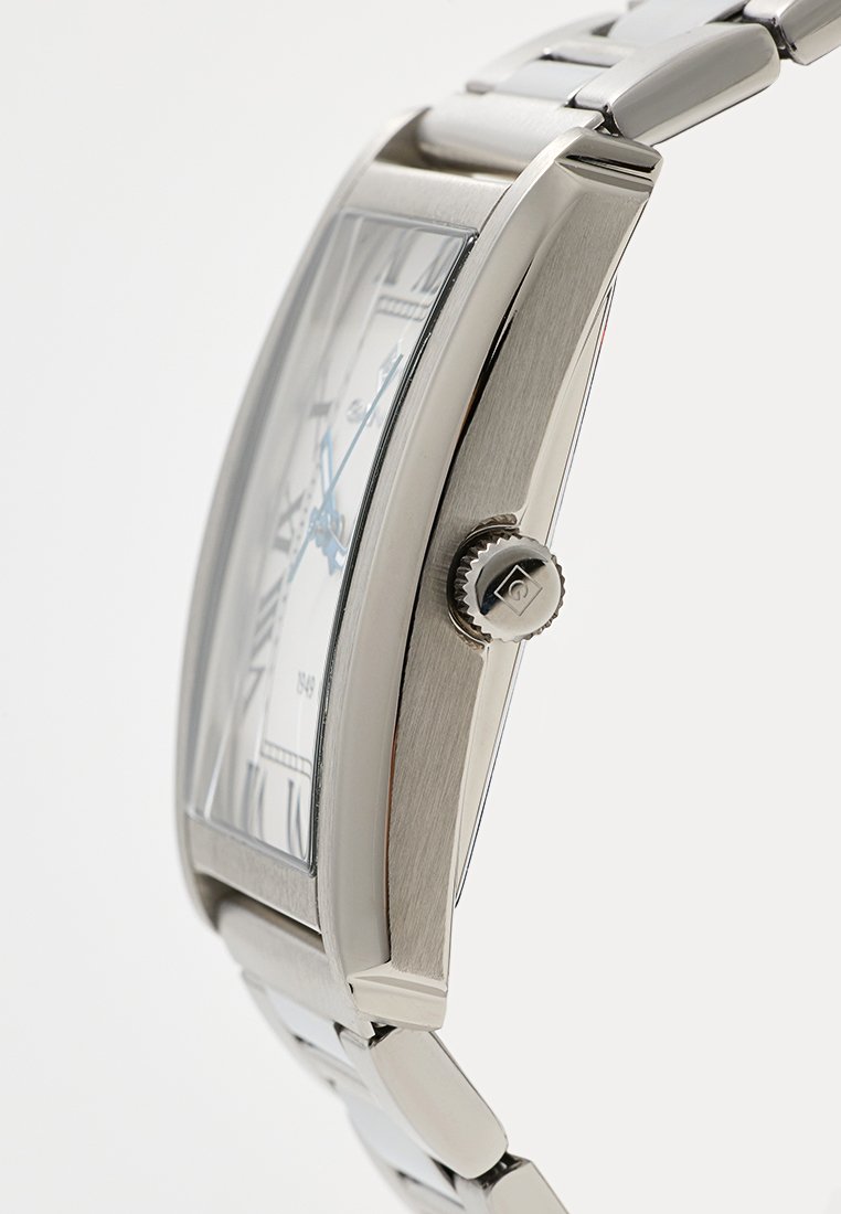 Montre en acier inoxydable argenté avec un boîtier rectangulaire, une lunette texturée et un cadran blanc avec des accents bleus et une couronne sur le côté.