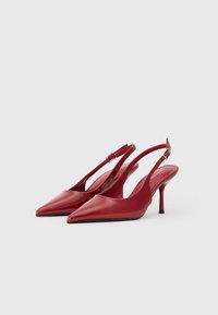 Escarpins en cuir verni rouge à dos ouvert, avec un bout pointu, un talon fin et un design découpé sur les côtés, dotés d'une bride cheville réglable.