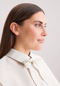 Camicia bianca con sottili righe blu, dotata di colletto a papillon e bottoni. Tessuto liscio e vestibilità su misura. Vista di profilo mostrata.