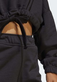 Svart kort sweatshirt med dragsko i midjan och elastiska ärmslut, tillsammans med matchande joggers. Mjuk textur och avslappnad passform.