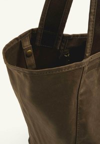 Brown canvas tote bag with sturdy, textured fabric, featuring a prominent zip pocket inside and reinforced fabric straps.