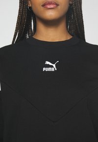 Zwarte sweatshirt met een ronde hals, voorzien van een witte geborduurde Puma-logo. Het ontwerp omvat een gestructureerd V-vormig patroon op de voorkant.