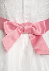 Bílé krajkové šaty s vrstvenou tylovou sukní, v pase mají širokou růžovou saténovou mašli, která je vázaná uzlem ve středu.