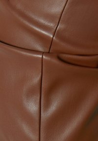 Superficie in pelle marrone con una texture liscia e una leggera lucentezza, con cuciture e pieghe visibili che arricchiscono il dettaglio del design.