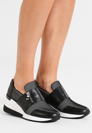Baskets à enfiler noir et blanc avec une tige en maille, des accents en cuir, une semelle blanche épaisse et un design de sangle contrastante distinctif.