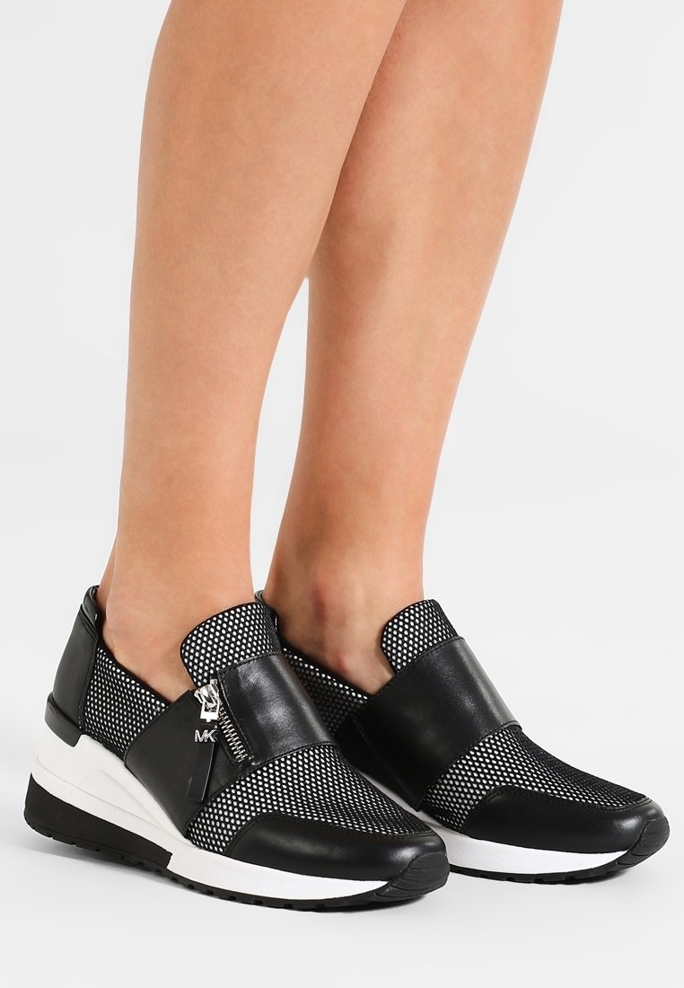 Sneaker slip-on in bianco e nero con una parte superiore in rete, particolari in pelle, una suola spessa bianca e un design distintivo della fascia a contrasto.