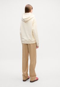 Sweatshirt crème avec une grande capuche, associé à un pantalon beige à jambes larges. Comprend des chaussures slip-on roses avec un motif distinct.