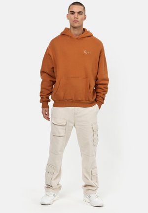 Oransje hettegenser med kengurulomme og hvit logo. Kombinert med beige cargobukser med flere lommer og en avslappet passform.