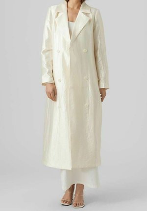 Lang, dubbelzijdig jasje van glanzend, licht ivoorkleurig stof. Voorzien van scherpe revers, lange mouwen en grote knopen. Glad textuur.