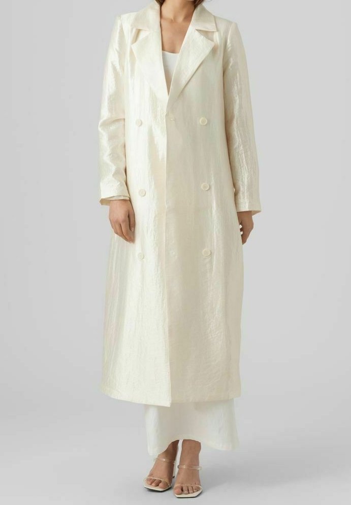 Lång, dubbelknäppt kappa i glänsande, ljus elfenbensfärgad tyg. Har spetsiga slag, långa ärmar och stora knappar. Slät textur.