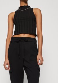 Svart kort tanktopp med vertikala ränder, scalloped halsringning och ett silverkedjeaccent. Kombinerad med svarta cargobyxor.