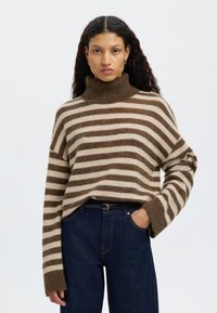 Vastag garbó pulóver barna és bézs csíkokkal; puha, texturált anyagból készült; laza szabás széles ujjakkal. Sötét farmernadrággal párosítva.