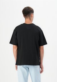 Black short-sleeve t-shirt with a crew neck, made of cotton. Features a relaxed fit and simple back design, paired with light blue jeans.