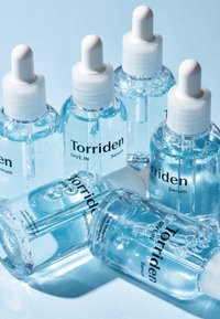 Klare glasserumflasker med hvide pipetter, der viser blå væske og sort tekst. Forskellige vinkler og bobler er synlige.