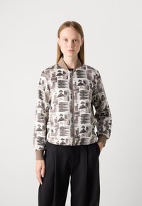 Giubbotto bomber con sfondo beige, caratterizzato da una stampa astratta ripetitiva in marrone e nero. Dettagli con polsini e colletto a coste. Chiusura con zip.