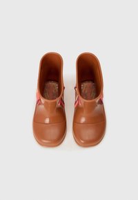 Bottes en caoutchouc marron avec une texture lisse, larges ouvertures et un accent décoratif en rose et jaune sur les côtés. L'intérieur présente un motif coloré.