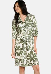 Abito camicia con colletto in crema con una stampa floreale verde. Presenta una vita con cintura, maniche a tre quarti e una chiusura tramite bottoni frontale.