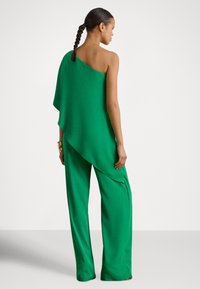 Macacão verde assimétrico em tecido fluido, com design de um ombro só e calças largas. Textura suave com detalhes mínimos.