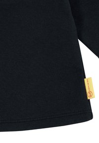 Zwarte katoenen langslijfshirt met een zijlabel met gele achtergrond en rode tekst. Gladde structuur en rechte zoom.