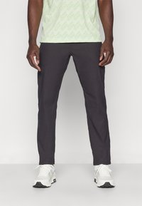 Pantalons noirs ajustés avec une texture lisse, associés à une chemise à motif vert clair et des baskets blanches avec des accents noirs.
