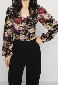 Top corto nero floreale con maniche a sbuffo, caratterizzato da fiori rosa e borgogna, abbinato a pantaloni attillati neri a vita alta.