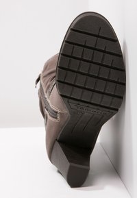 Bota de ante marrón hasta el tobillo con suela de goma texturizada, detalle de cremallera lateral y tacón bloque ligeramente elevado. Etiqueta que dice "Tamaris 36."