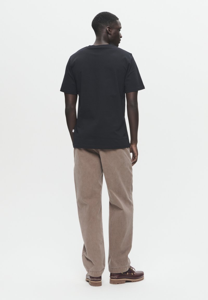 Schwarzes Baumwoll-T-Shirt mit lockerer Passform, kurzen Ärmeln und Rundhalsausschnitt, kombiniert mit hellbraunen Cordhosen und braunen Schuhen.