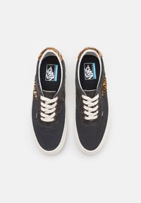 Baskets Vans noires avec lacets blancs, doublure en fourrure imprimé léopard et semelles blanches, vues de dessus sur un fond blanc.