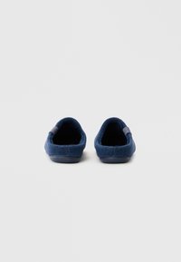 Pantofole in feltro navy con una texture morbida, tallone arrotondato e suola in gomma. Presentano un piccolo dettaglio laterale per facilitare l'indossamento.