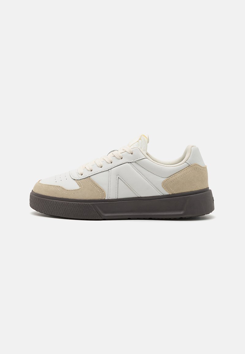 White and beige sneaker with a leather and suede upper, round toe, lace-up design, and textured black rubber sole.