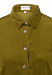 Camicia in velluto a coste verde oliva con colletto a punta, caratterizzata da quattro grandi bottoni, una tasca sul petto e una texture a coste verticali.