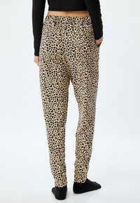 Loungebroek met luipaardprint, voorzien van een elastische tailleband, taps toelopende pijpen en een zachte stoftextuur. Kleurenpalet bevat beige, zwart en bruin.