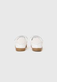 White sneakers with a rubber sole, nubuck heel, and soft fabric lining. Back view shows a simple design and rounded edges.
