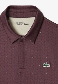 Bordowa koszulka polo z teksturowanym wzorem, krótkim rękawem i zapięciem na guziki przy kołnierzyku. Posiada zielono-białe logo Lacoste. Regularny krój.