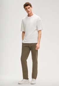 Luźna biała bawełniana koszulka z krótkim rękawem, w połączeniu z oliwkowozielonymi spodniami i białymi trampkami. Prosty design, gładka faktura.