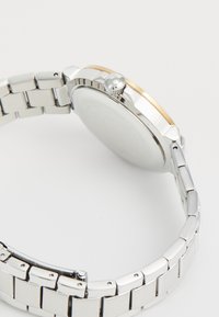 Silver metal wristwatch with a smooth, circular case and gold accent. Features a link bracelet and a crown on the side for adjustment.