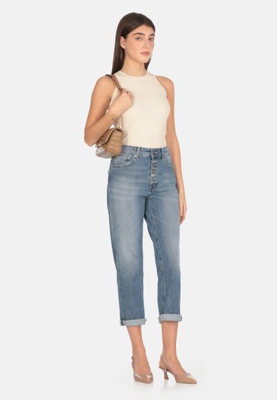 Top bianco a coste senza maniche, jeans azzurri a vita alta con bottone davanti e risvolto, e scarpe beige con tacco a blocco. Borsa marrone con tracolla a catena.