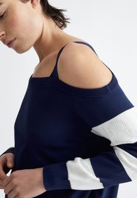 Maglione navy con spalle scoperte e maniche bianche a motivo. Presenta polsini a costine e una vestibilità aderente, realizzato in un morbido materiale a maglia.