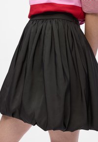 Svart skjørt med et samlet design, som har folder og en glatt tekstur. Midjen er tilpasset, noe som komplementerer den runde hemline.