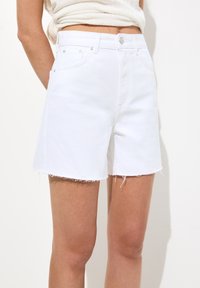 Vita denimshorts med fransad nederkant, med hög midja, framfickor och knäppning. Slät textur och rena linjer.