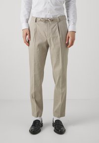 Smėlio spalvos linijiniai kelnių su klostėmis priekyje, elastinga juosmens juosta ir raišteliu. Dėvimi su balta elegantiška marškinėliais ir juodais loafer'iais, papildyti baltais kojiniais.