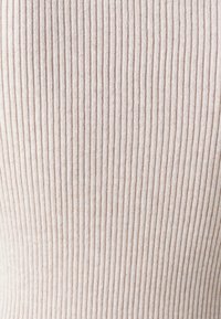 Gros plan d'un tissu tricoté côtelé beige montrant des lignes texturées verticales et des détails de matériau doux.