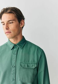 Grüne Hemdjacke aus leichtem Stoff, mit klassischem Kragen, einer Brusttasche und einer glatten Textur.