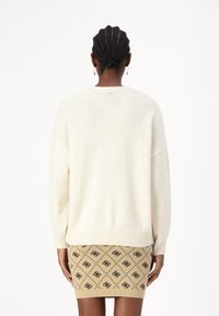 Kremowy, oversize'owy sweter z prążkowanymi mankietami, zestawiony z beżową, dopasowaną spódnicą z geometrycznym czarnym wzorem.
