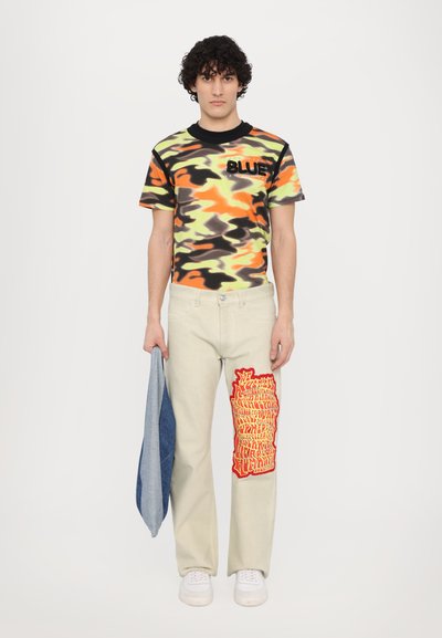 Multicolored camouflage shirt with "BLUEY" text, paired with cream-colored pants featuring a large red graphic design on the leg.