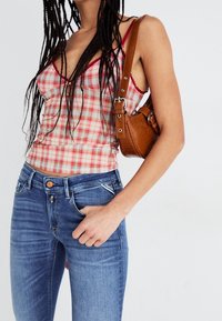 Top corto de cuadros rojos y rosas con tirantes finos, combinado con jeans ajustados azules. Se lleva un bolso de mano marrón con estampado de cocodrilo en el hombro.