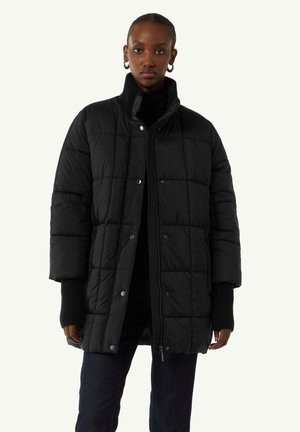 Schwarze Steppjacke mit einem gesteppten Design, hohem Kragen und Druckknopfverschluss. Die Ärmel sind leicht übergroß und gerippt.